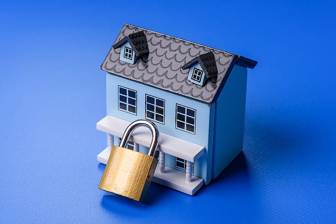 A small figure of a house with a golden padlock as a concept of home security.